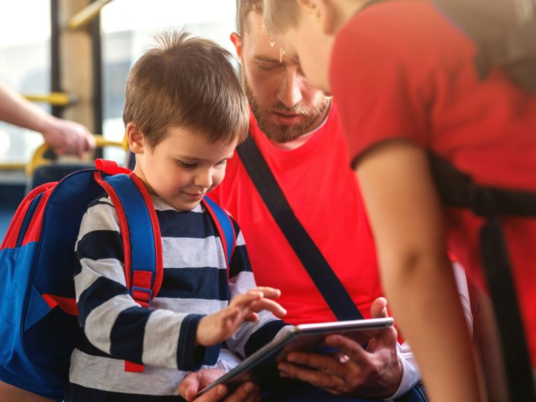Vater und Sohn sitzen gemeinsam im Bus und bedienen ein Tablet – OWLmobil sorgt für eine verlässliche Verbindung dank Mobilitätsgarantie.